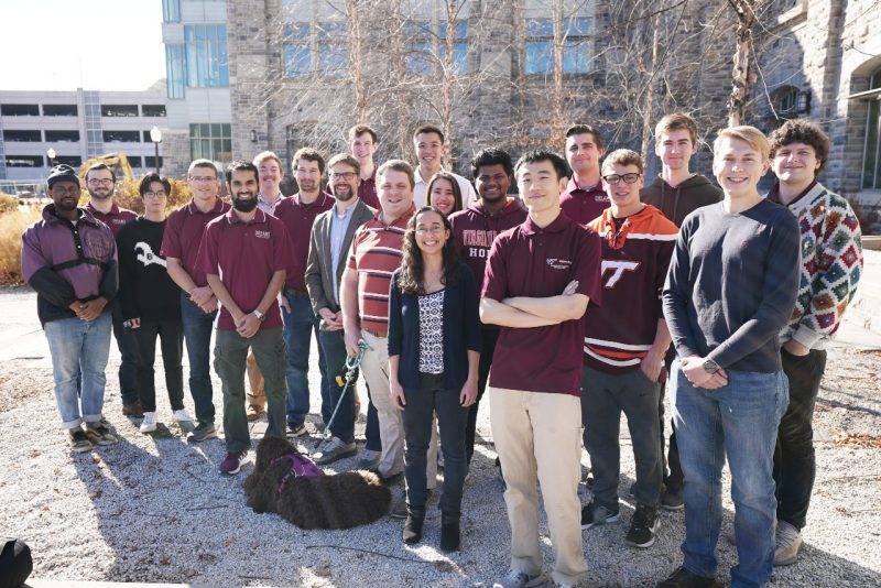 Twenty member of the dreams lab and a dog wearing mostly maroon standing in a gravel patio.